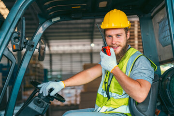 A man in a yellow safety vest and a hard hat is sitting in a forklift cab © chokniti