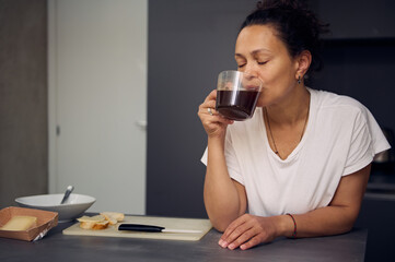 Portrait of relaxed happy woman in pajamas, taking a sip of freshly brewed espresso coffee during...