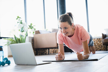 Closeup young woman standing in plank position while watching online training on laptop at home....
