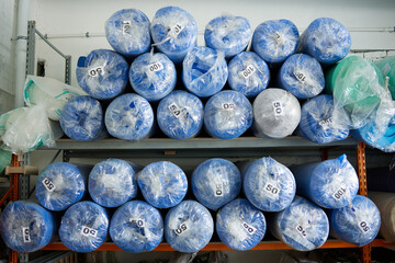 On the rack there are rolled sheets of blue foam rubber, packed in film. Warehousing of production parts in a furniture factory
