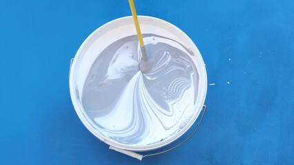 Three colors of paint are mixed in bucket of paint with mixer.