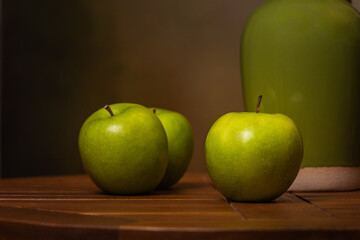 green apples with green ceramic pitcher on wooden table with brown background