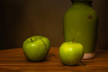 green apples with green ceramic pitcher on wooden table with brown background