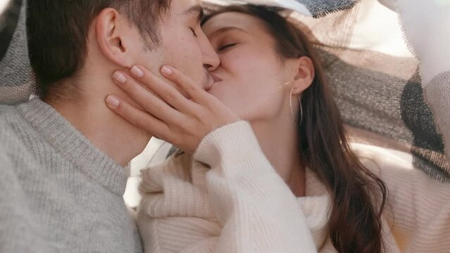 A happy couple shares an intimate moment, laughing and kissing under a plaid blanket, enjoying a sunny day outdoors with love and affection.