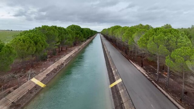 High-speed drone flight over the Tajo-Segura water transfer canal in Spain and hovering over it showing a grove of trees next to the canal