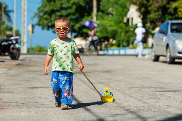 a boy with glasses walks down the street, a boy leads a car by a string, a child walks, carousel for kids, childhood in Cuba,