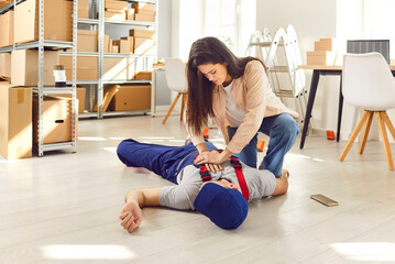Young woman giving first aid to Injured unconscious worker lying on the floor on workplace in...
