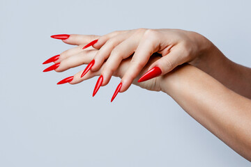Closeup of  elegant female hands with red stiletto nails on gray background