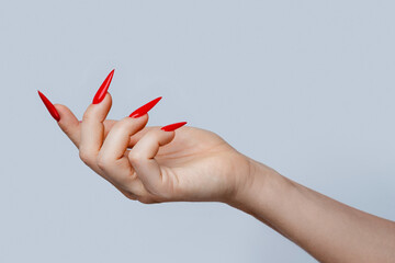 Closeup of  elegant female hand with red stiletto nails on gray background