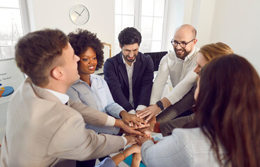 Diverse business people men and women putting their arms together sitting in a circle in office....