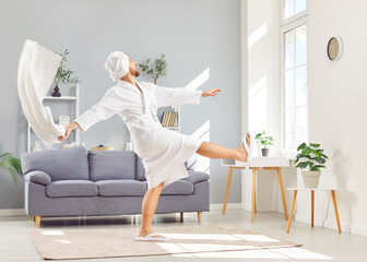 Smiling and happy man in a bathrobe with a towel on head is dancing to music in the morning....