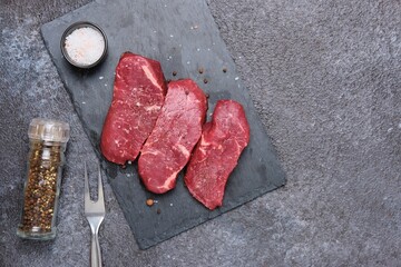 Raw steak Striploon on a shale board on a black concrete background. Types of beef cuts for steaks.