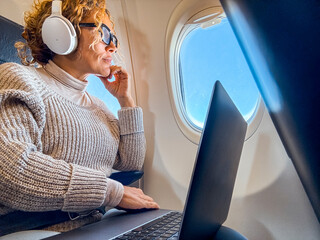 Middle aged business woman working on laptop while sitting on airplane. Travel and business trip lifestyle female people using computer and looking outside the window