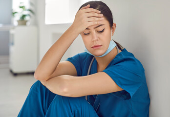 Portrait of sad, exhausted, stressed woman nurse, doctor, medical worker in blue scrubs sitting on...