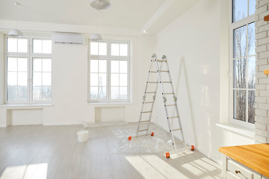 Step ladder and paint bucket standing in empty light room in new house or flat with freshly painted white walls with copy space. Renovation process in apartment. Home repair and moving day concept.