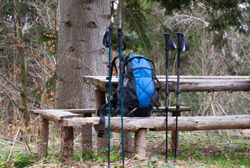 backpack and trekking poles on a wooden bench in the forest