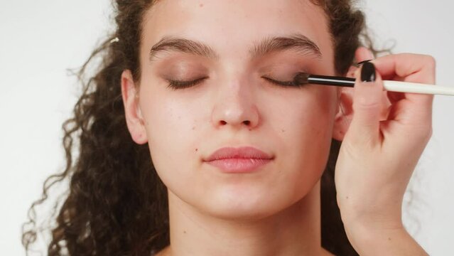 Eye shadow makeup to the upper eyelid, close-up. Makeup artist applies a bright eye shadow with a make-up brush.Tutorial master class of professional makeup, smoky eyes 
