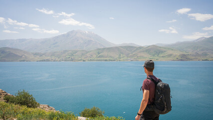 Young athletic man with backpack enjoying views on beautiful lake with mountains in backdrop, Turkey