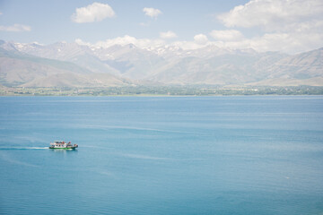 Sightseeing boat with tourists sailing on beautiful blueish lake with mountains in backdrop, Turkey