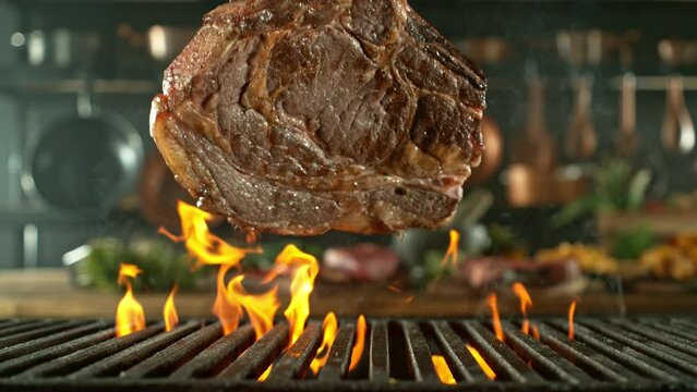 Close-up of tasty beef steak on cast-iron grate with fire flames, super slow motion, filmed on high speed cinematic camera at 1000 fps. Camera movement.
