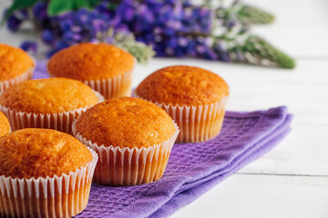 Delicious muffins and purple lupine flowers on white wooden background.