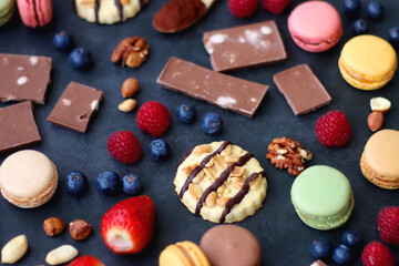 Macarons, chocolate, cookies, berries and various nuts on dark blue background. Selective focus.