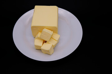 Butter is placed on white plate with a black background. A block of butter with a dark background. Fresh ingredient for baking and home cooking. Close-up butter texture of food image with copy space.