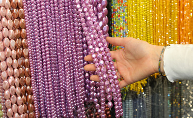 Girl while choosing a pearl necklace among many hanging in the fashion accessories stor - 785638379