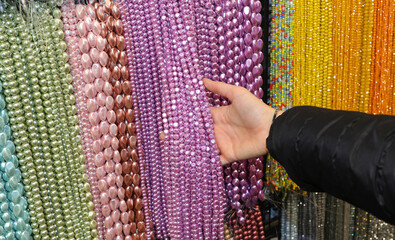 hand choosing a pearl necklace among many hanging in the fashion accessories store in the shopping...