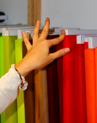 hand of a girl choosing crimson red color fabric in the haberdashery - 785638930