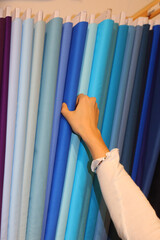 hand of a young girl choosing blue color fabric in the haberdashery with many colorful fabrics - 785639125