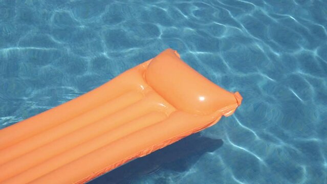 Slow motion video of orange float floating through the water of a pool in sunlight