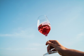 Female hand delicately holds a glass of rose wine against blue clear sky