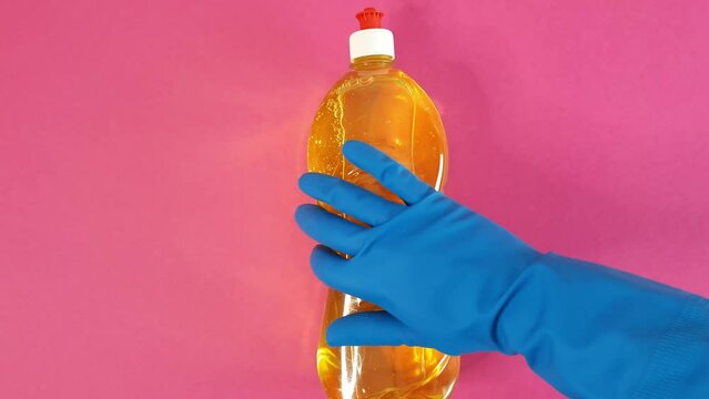 Hand in blue rubber glove picks up bottle of household chemicals from pink table. person takes detergent liquid. Cleaning Services Concept - house, apartment, office cleaning. Template with copy space