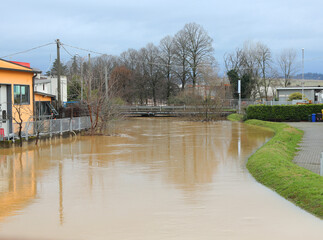 Fototapeta premium Swollen river flooded after the flood in the industrial area with warehouses at risk of flooding