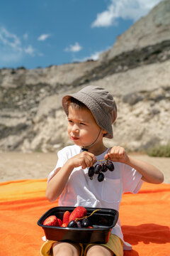 Adorable boy in a bucket hat eats fruits and enjoys a sunny beach picnic
