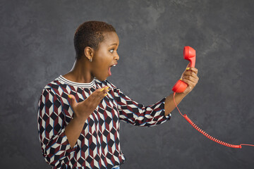 Wow. Excited black woman who got amazing news looking at red fixed land line cord phone receiver...