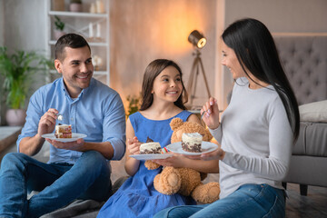 Happy caucasian young family enjoying the cake at home. Cheerful family talking and having fun party while eating birthday cake. Man woman and daughter girl celebrating mothers fathers day together