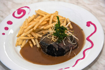 Plate of black pudding in mushroom sauce and French fries on restaurant table, food