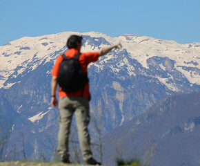male hiker pointing at snowcapped mountains with backpack on during high altitude hike - obrazy, fototapety, plakaty