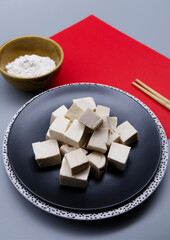 Tofu on black plate with red and grey background. Traditional Chinese food and red color conveys good luck. Fresh tofu texture. Cooking healthy soft tofu for vegan with two colored backgrounds.