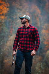 Handsome Lumberjack in Red Checkered Shirt with Axe in Autumn Foggy Forest - 785649120