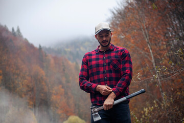 Handsome Lumberjack in Red Checkered Shirt with Axe in Autumn Foggy Forest - 785649592