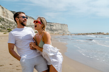 Young attractive couple laughs as they walk along the beach