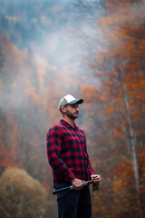 Handsome Lumberjack in Red Checkered Shirt with Axe in Autumn Foggy Forest - 785649768