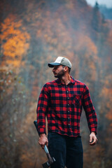 Handsome Lumberjack in Red Checkered Shirt with Axe in Autumn Foggy Forest - 785651112