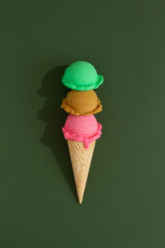 Triple-layered ice cream cone with colorful scoops in green background