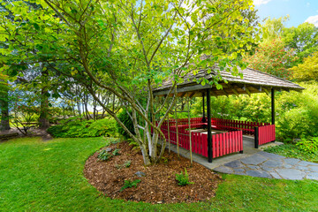 A small red gazebo in a lush formal lakeside garden in New Denver, BC, Canada.