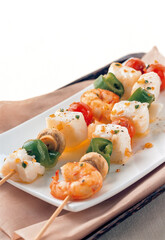 two skewers of seafood, fish and vegetables on white plate