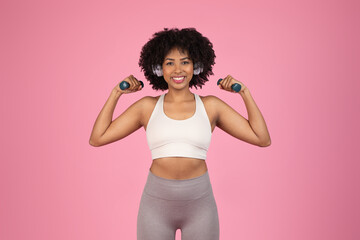 Smiling woman flexing with dumbbells on pink background